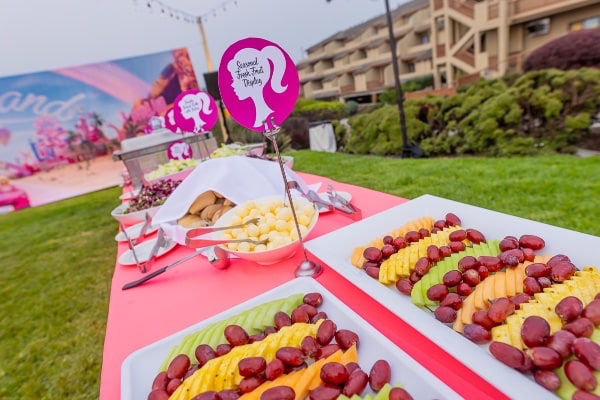 A buffet of fruit and desserts on a table in front of a sign.